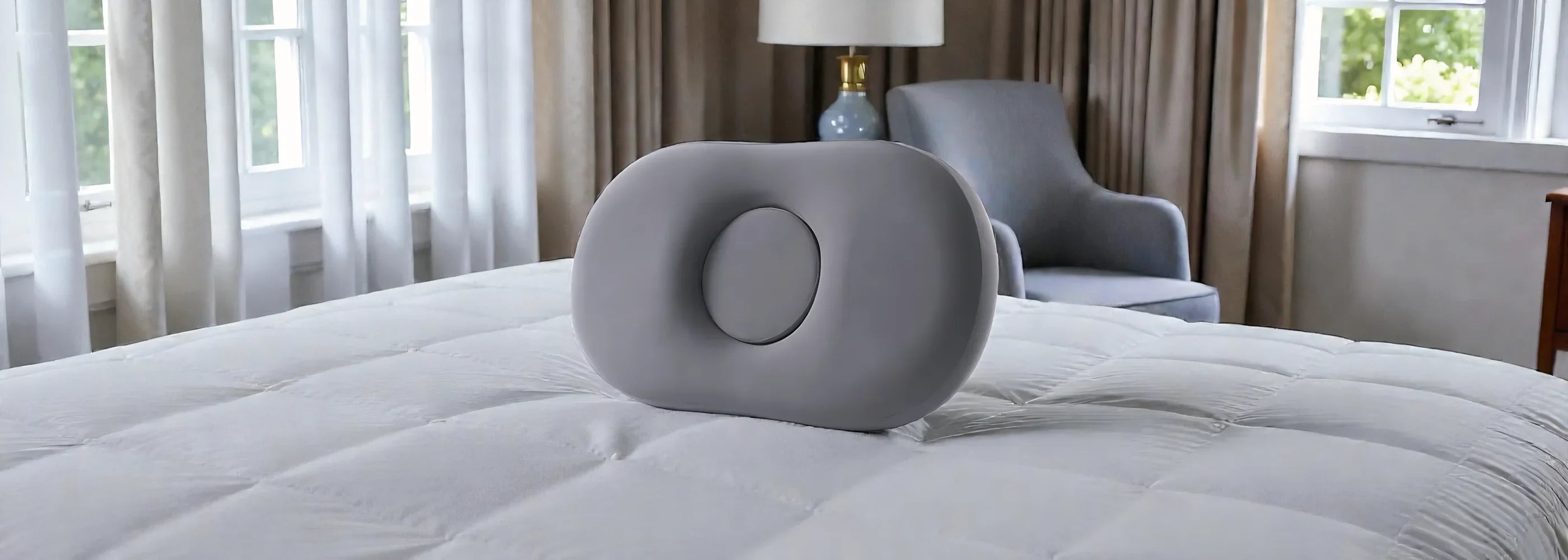 Gray orthopedic pillow with a central depression on a white quilted bed in a bright bedroom